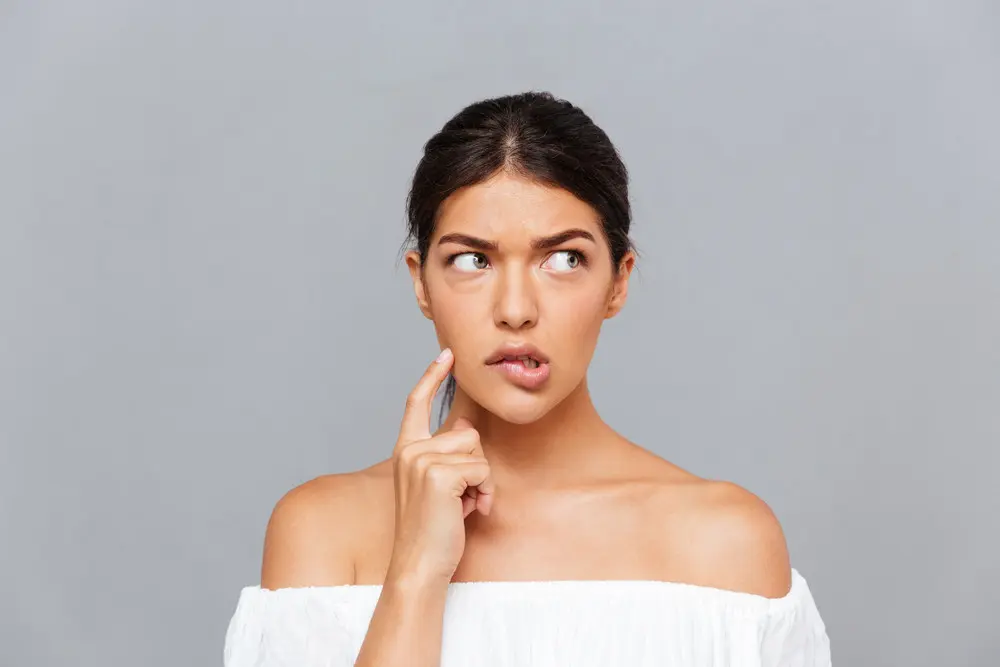 Close-up portrait of a pensive pretty girl thinking about something isolated on the gray background